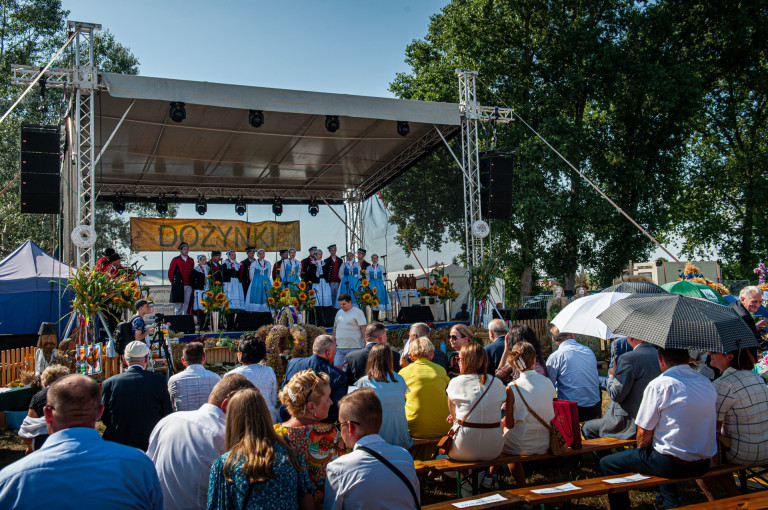Na scenie śpiewają członkowie zespołu ludowego. Przed sceną siedzą goście.