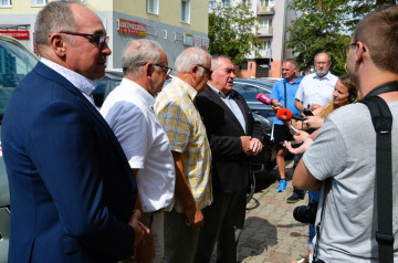 Grupa mężczyzn stoi na parkingu. Starosta koniński udziela wywiadu dziennikarzom.