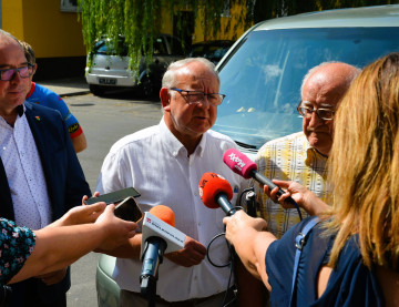 Przewodniczący rady powiatu udziela wywiadu dziennikarzom przed zaparkowanym busem.