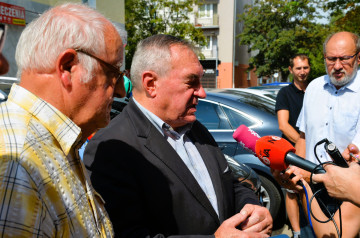 Grupa mężczyzn stoi na parkingu. Starosta koniński udziela wywiadu dziennikarzom.