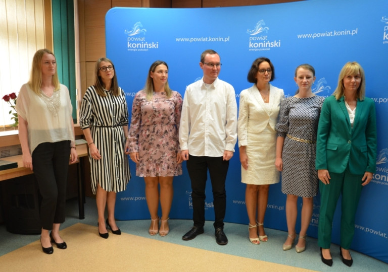 Sześć nauczycielek i jeden nauczyciel stoją w sali konferencyjnej na tle niebieskiego baneru.