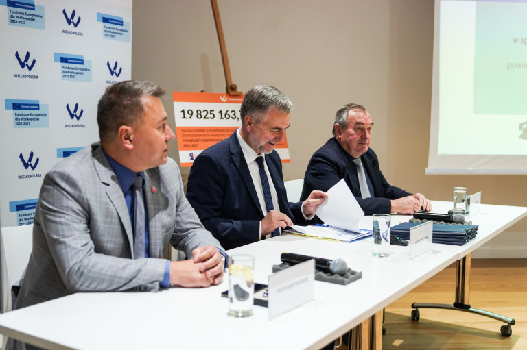 Trzech mężczyzn siedzi przy stole i podpisuje dokument.