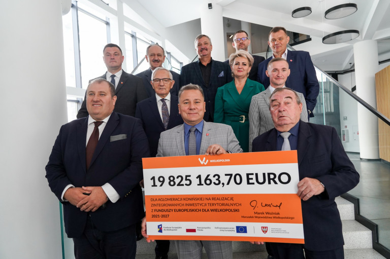 Jedenaście osób stoi na schodach. Dwóch mężczyzn trzyma w rękach symboliczny czek.