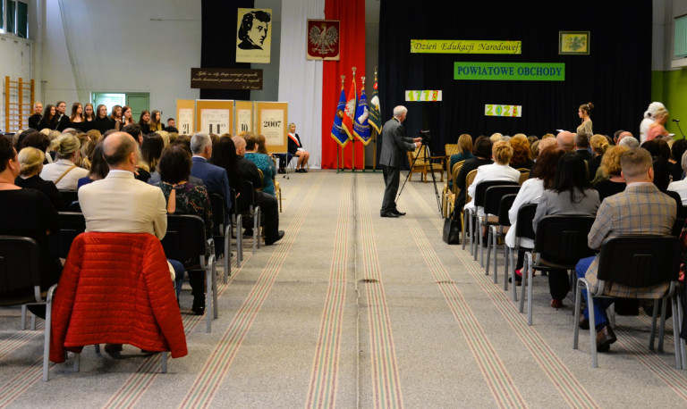 Zaproszeni goście siedzą na krzesłach po lewej i prawej stronie sali.