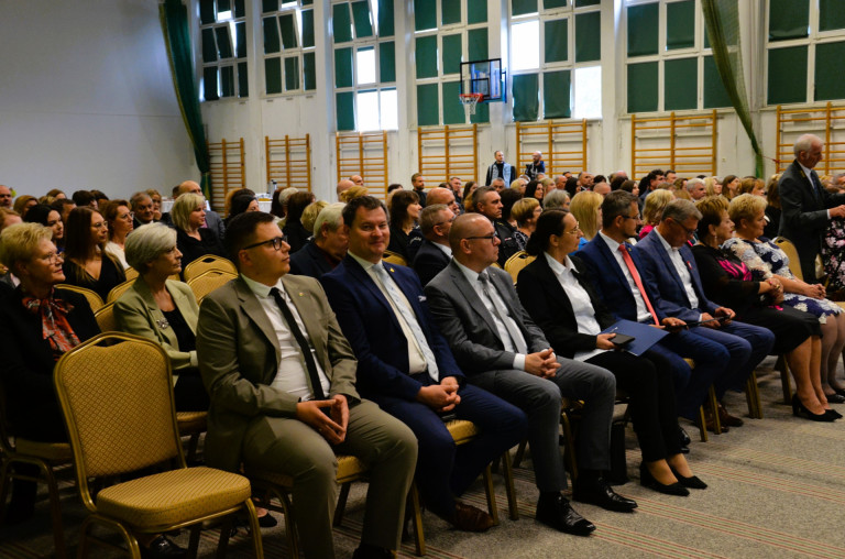 Gospodarze uroczystości i zaproszeni goście siedzą na żółtych krzesłach.