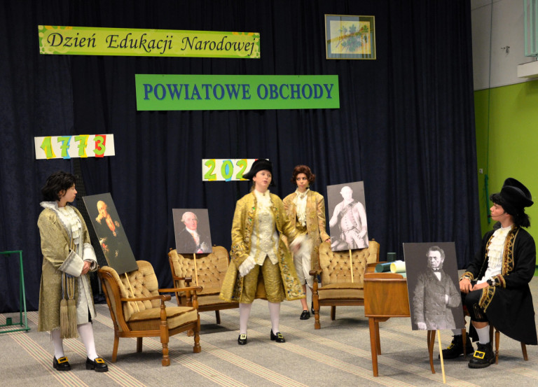 Czworo uczniów ubranych w stroje z epoki oświecenia ogdrywa role w przedstawieniu.
