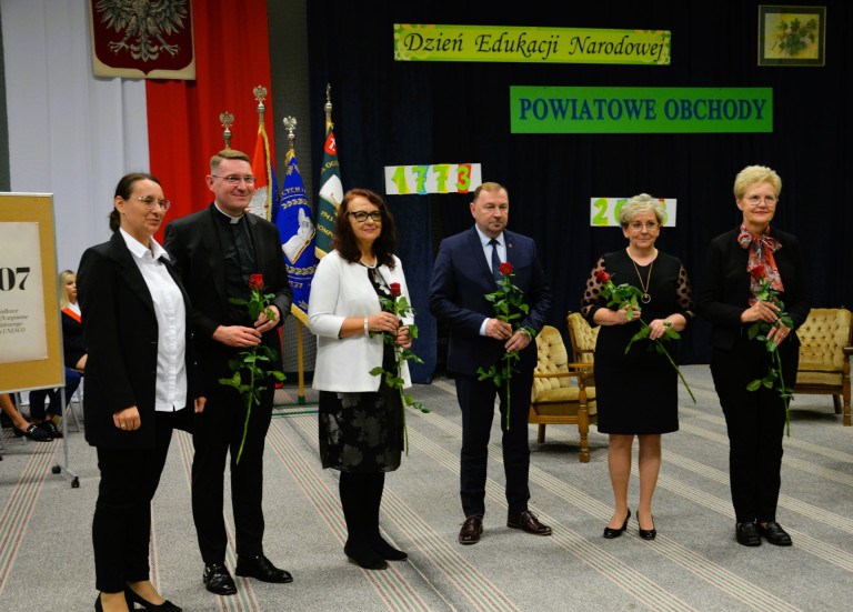 Kobieta oraz wyróżnione osoby z różami - trzy kobiety i dwóch mężczyzn - stoją obok siebie.