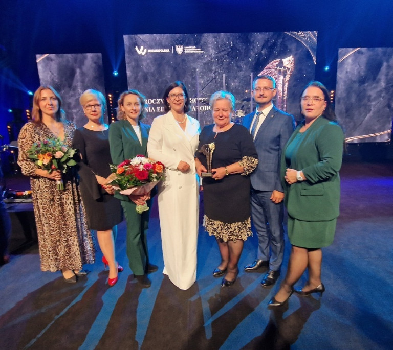Sześć kobiet i jeden mężczyzna stoją w rzędzie. Dyrektorka szkoły trzyma statuetkę.