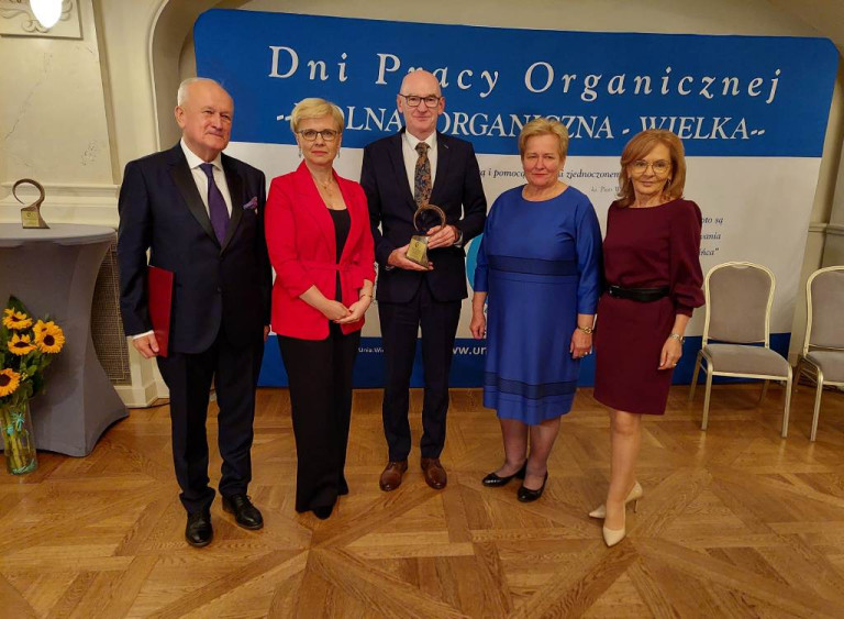 Trzy kobiety i dwóch mężczyzn stoją obok siebie w rzędzie. Jeden mężczyzna trzyma statuetkę.