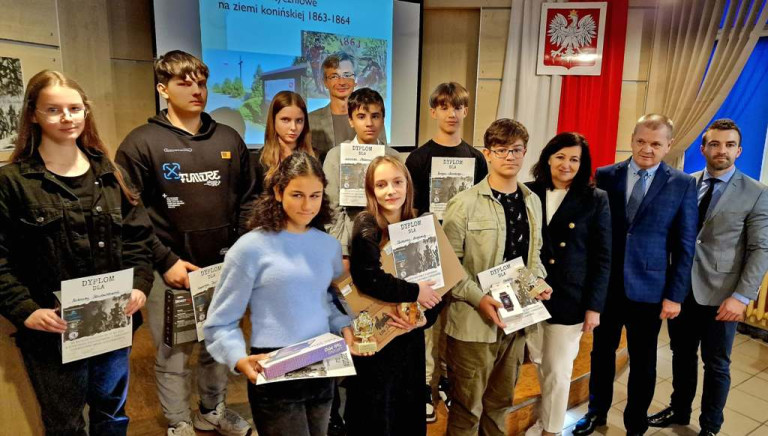 Nauczyciele i nagrodzeni uczniowie stoją z dyplomami i upominkami.
