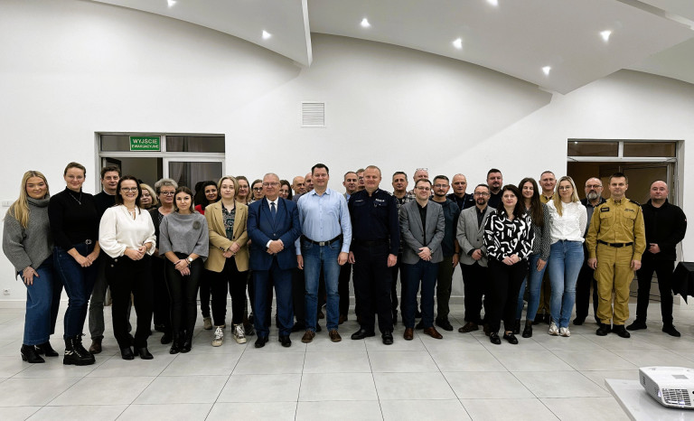 Sala. Kilkadzieścia osób. Uczestnicy szkolenia stoją, pozują do zdjęcia.