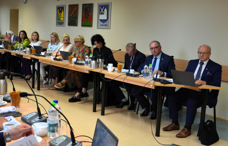 Grupa ludzi siedzi przy stołach w sali konferencyjnej.