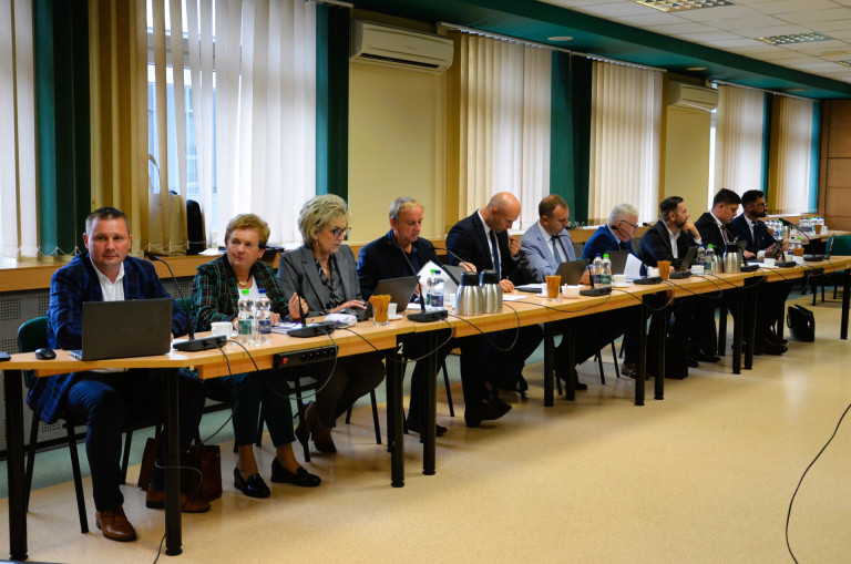 Grupa ludzi siedzi przy stołach w sali konferencyjnej.