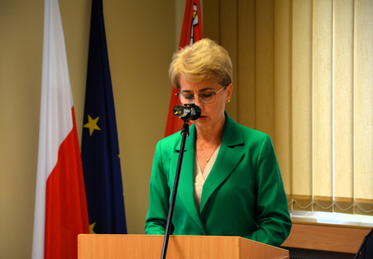 Kobieta w zielonej marynarce przemawia do mikrofonu.