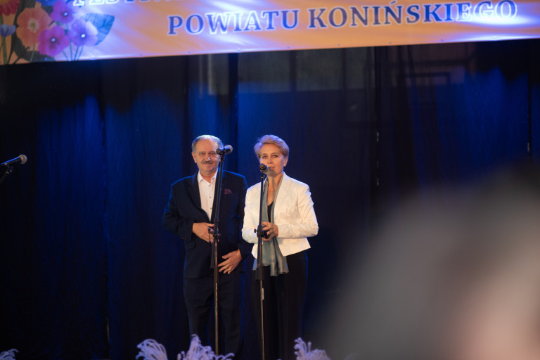 Kobieta w białej marynarce oraz mężczyzna w garniturze stoją na scenie.