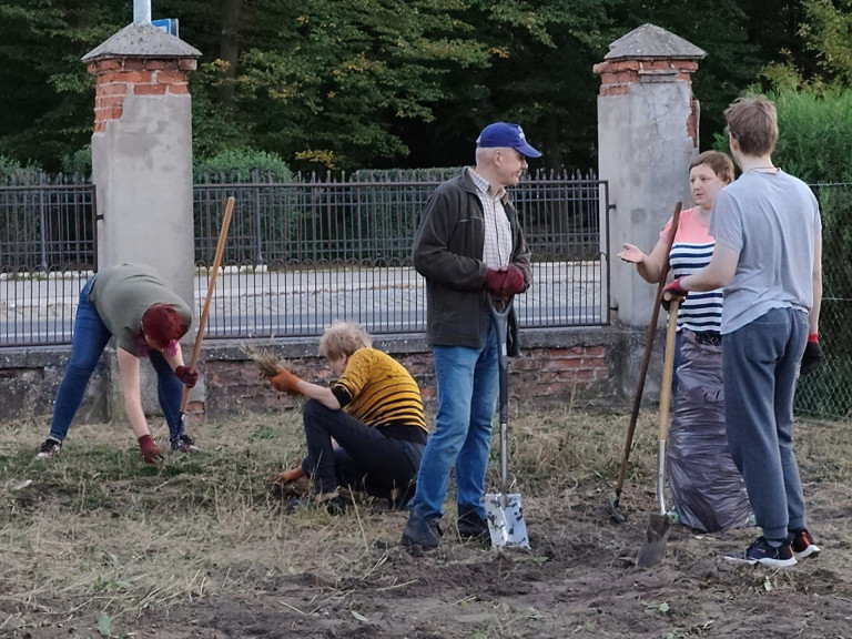 Grupa ludzi z narzędziami ogrodowymi.