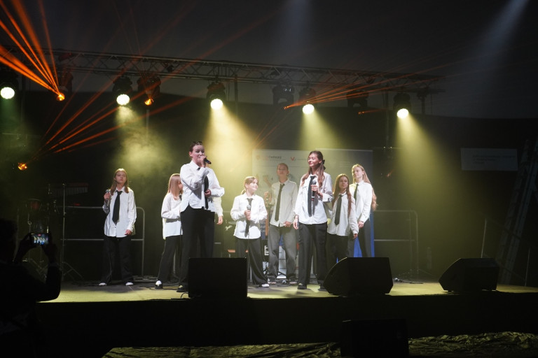 Grupa ludzi w białych koszulach występuje na scenie.