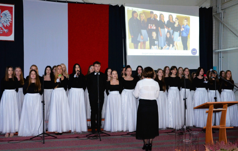 Grupa ludzi ubranych na czarno oraz biało występuje na scenie.