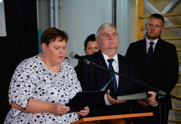 Kobieta i mężczyzna stoją przy mównicy. Kobieta przemawia do mikrofonu.
