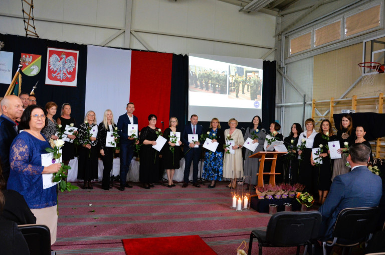Grupa ludzi stoi na scenie trzymając róże i dokumenty.