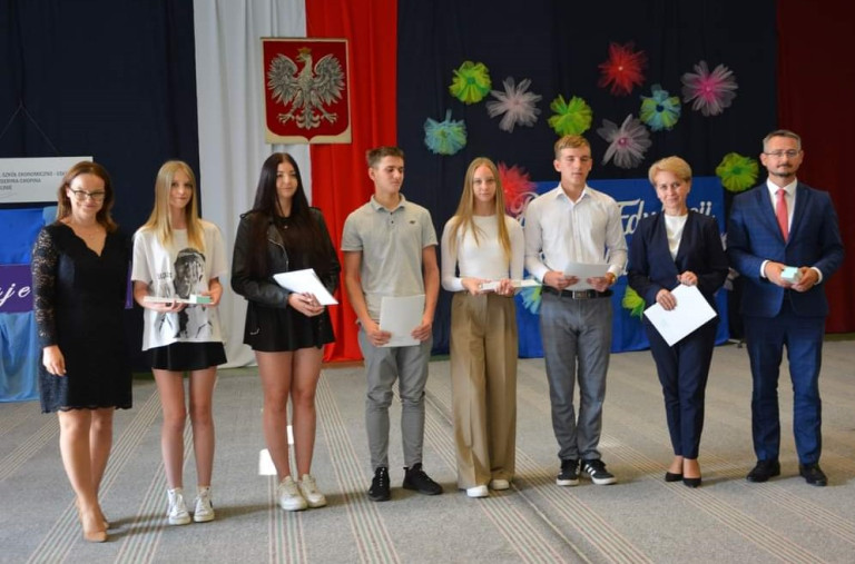 Grupa ludzi na tle godła. Część z nich trzyma dokumenty.