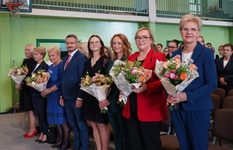 Grupa ludzi. Część z nich trzyma bukiety kwiatów.