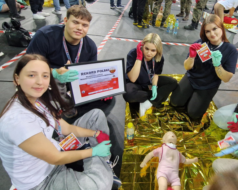 Grupa ludzi przy manekinie. Wśród nich mężczyzna trzymający dyplom.