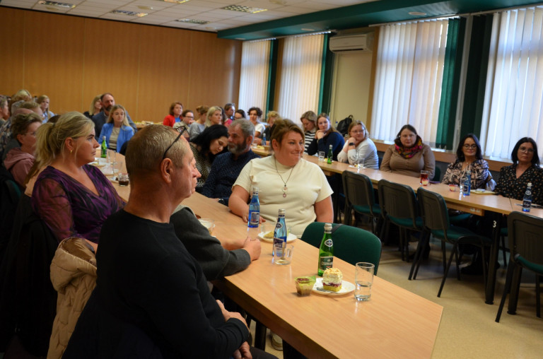 Grupa ludzi siedzi przy stołach w sali konferencyjnej.