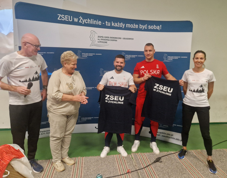Dwie kobiety i trzech mężczyzn. Dwóch mężczyzn ubranych jest w stroje sportowe.