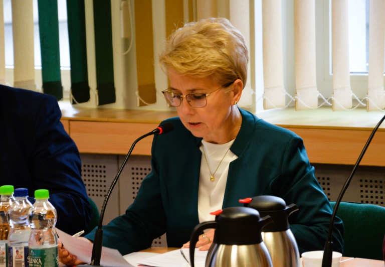 Kobieta w zielonej marynarce przemawia do mikrofonu.