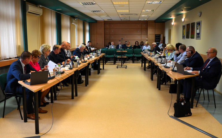 Grupa ludzi siedzi przy stołach w sali konferencyjnej.