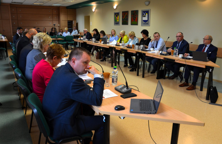 Grupa ludzi siedzi przy stołach w sali konferencyjnej.