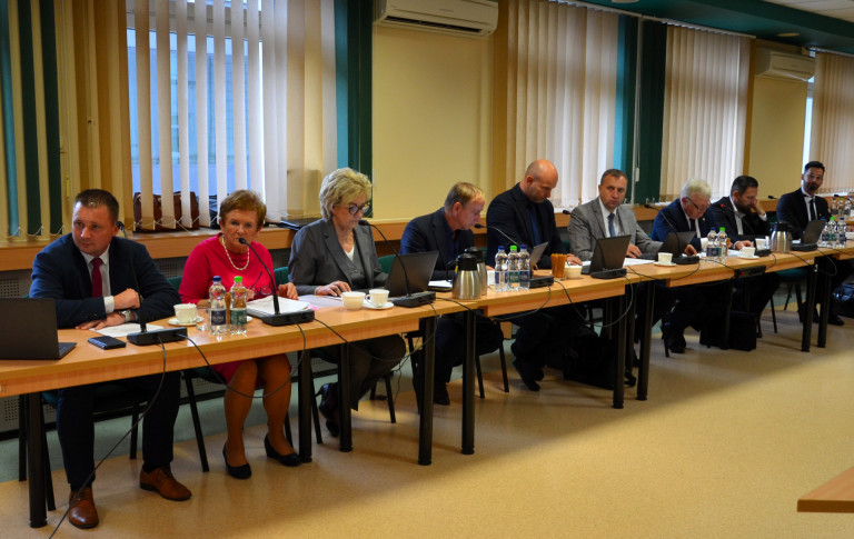 Grupa ludzi siedzi przy stole w sali konferencyjnej.