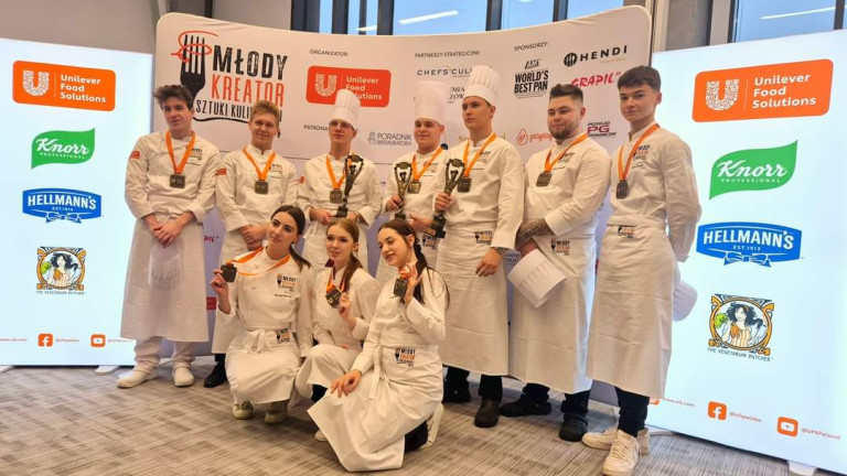 Grupa ludzi w białych fartuchach. Część z nich trzyma statuetki.