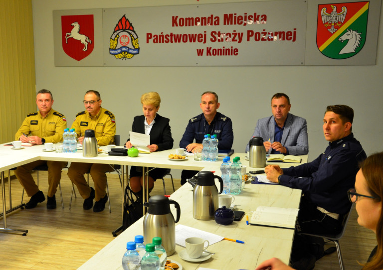 Ludzie siedzą przy stole. Część z nich ubrana jest w mundury.