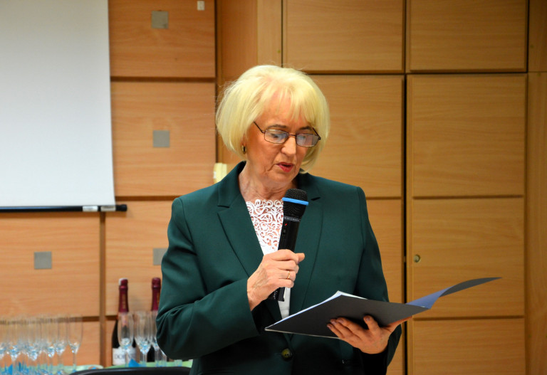 Kobieta w zielonej marynarce przemawia do mikrofonu.