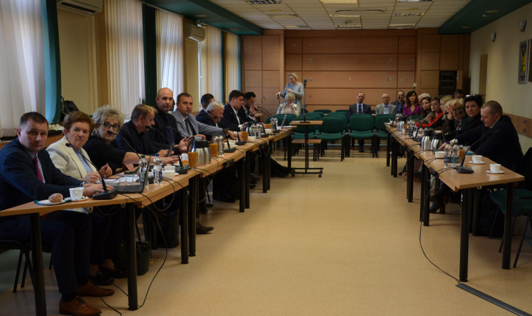 Grupa ludzi siedzi przy stołach w sali obrad.
