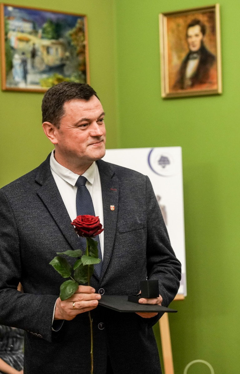 Mężczyzna w garniturze trzyma różę oraz dokument.