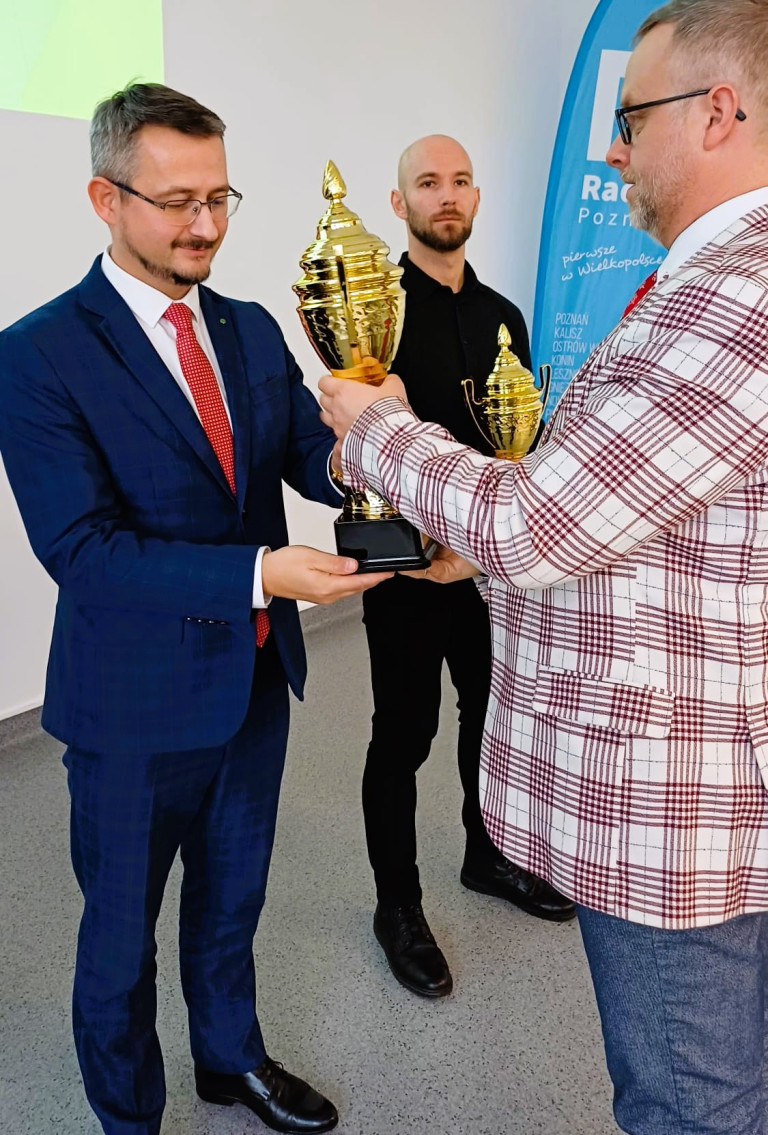 Mężczyzna wręcza puchar drugiemu mężczyźnie.