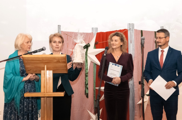 Cztery osoby stoją przy mównicy. Jedna z kobiet trzyma białą choinkę.