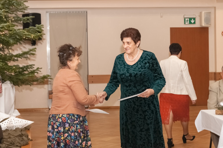 Kobieta w zielonej sukience podaje dłoń drugiej kobiecie.