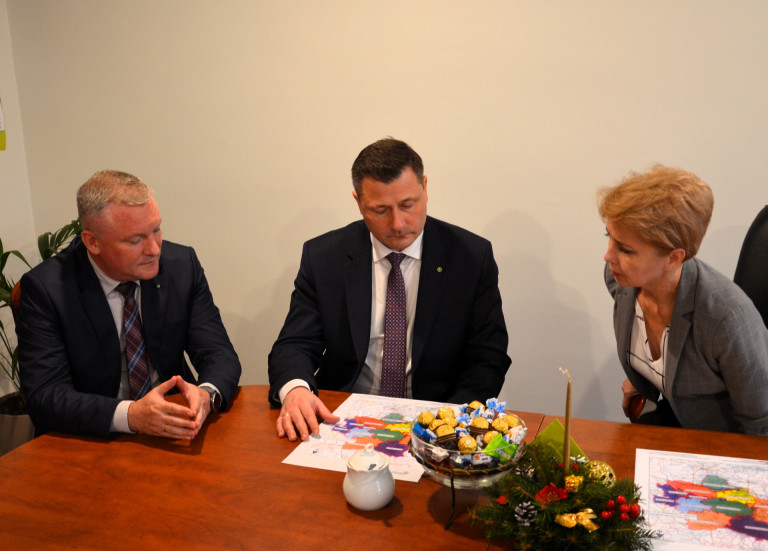 Kobieta i dwóch mężczyzn siedzą przy stole na którym leży mapa.