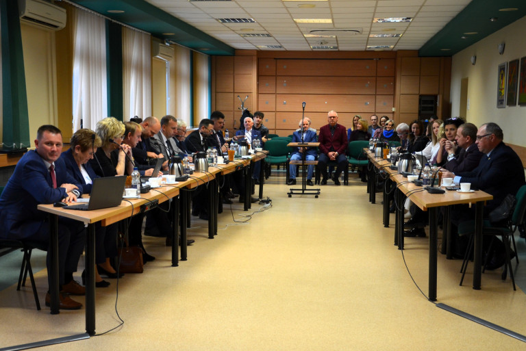 Grupa ludzi siedzi przy stołach w sali konferencyjnej.