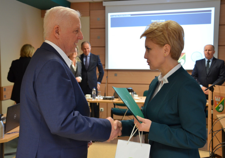 Mężczyzna uściska dłoń kobiety trzymającej torbę prezentową oraz dokument.