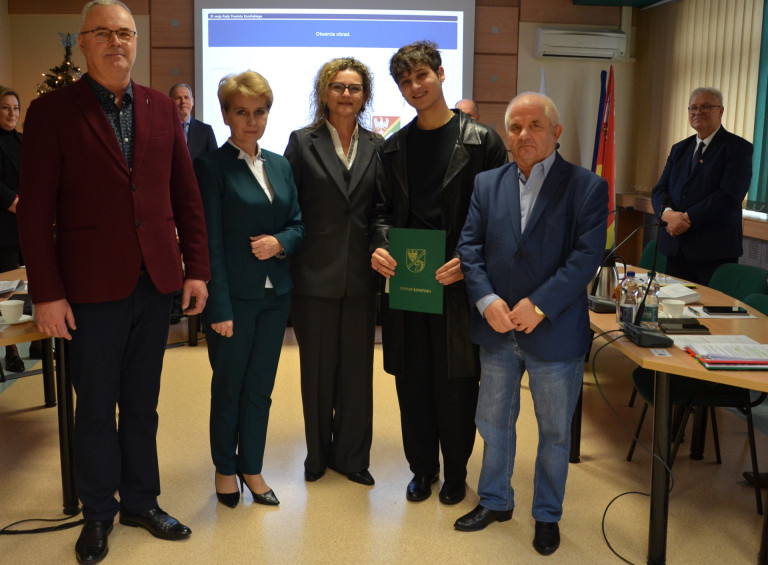 Grupa ludzi stoi w sali obrad. Jeden z mężczyzn trzyma dokument.