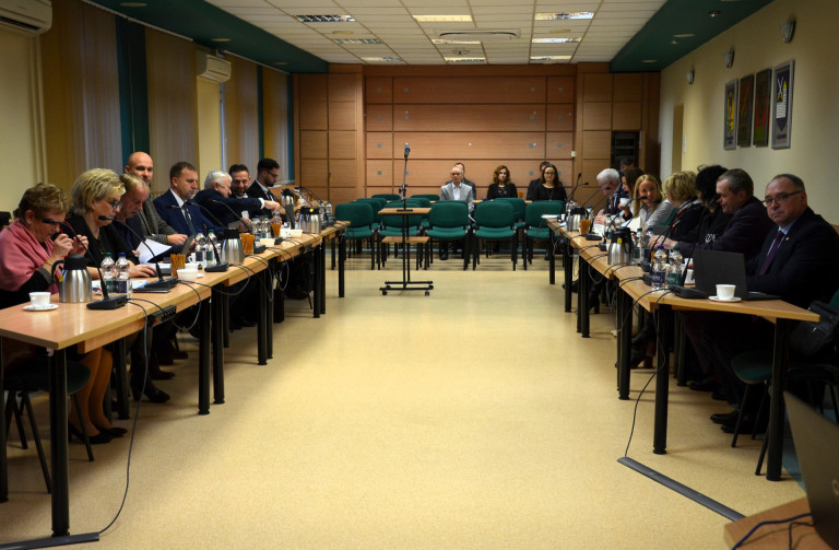 Grupa ludzi siedzi przy stołach w sali konferencyjnej.