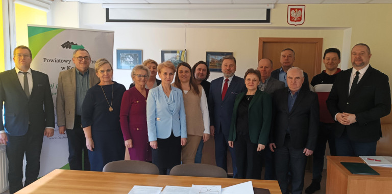 Grupa kobiet i mężczyzn stoi w sali.