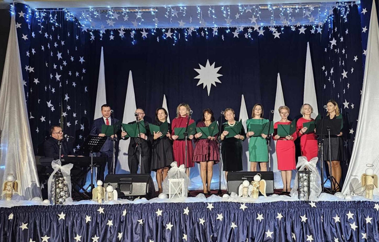 Grupa ludzi występuje na scenie ozdobionej świątecznymi dekoracjami.