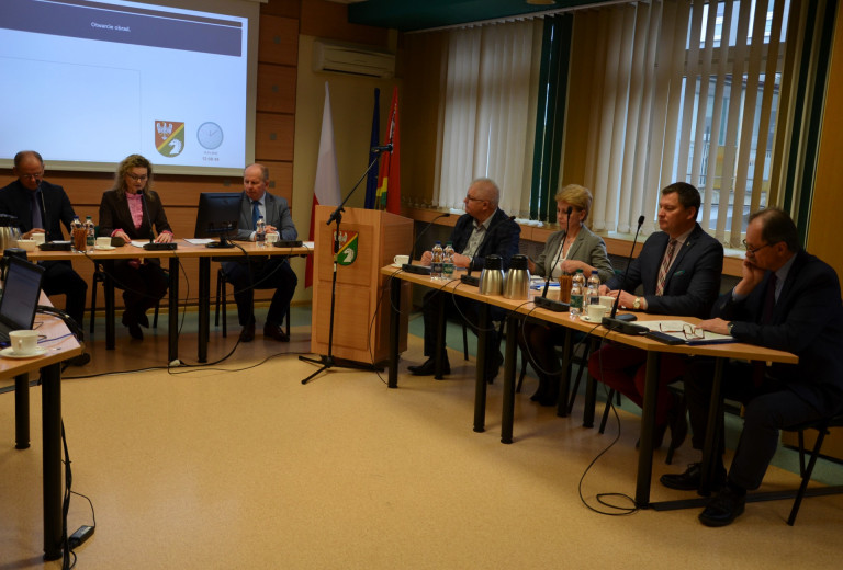 Grupa ludzi siedzi przy stołach w sali konferencyjnej.