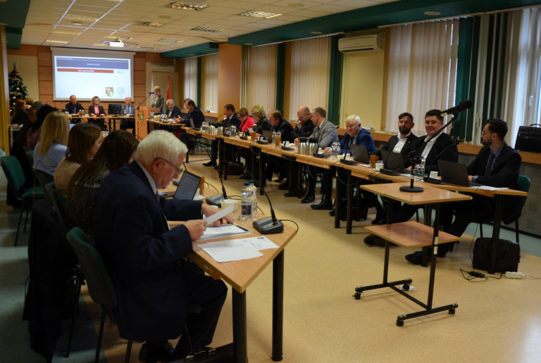 Grupa ludzi siedzi przy stołach w sali konferencyjnej.